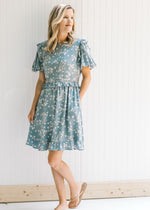 Model wearing a light blue dress with cream floral, bubble short sleeves and pockets. 