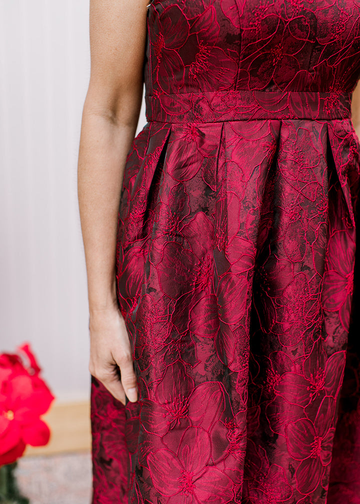 Close up of pleating as the waist of a wine colored dress with embroidered flowers and pockets. 