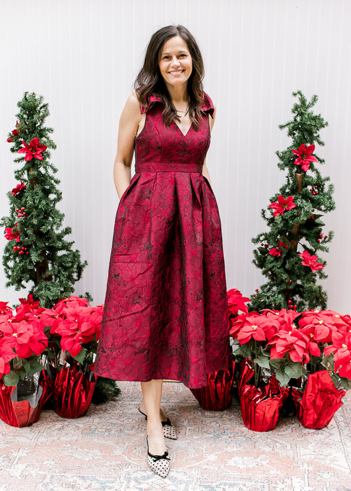 Model wearing heels and a sleeveless wine midi with embroidered floral, pleated waist and pockets. 