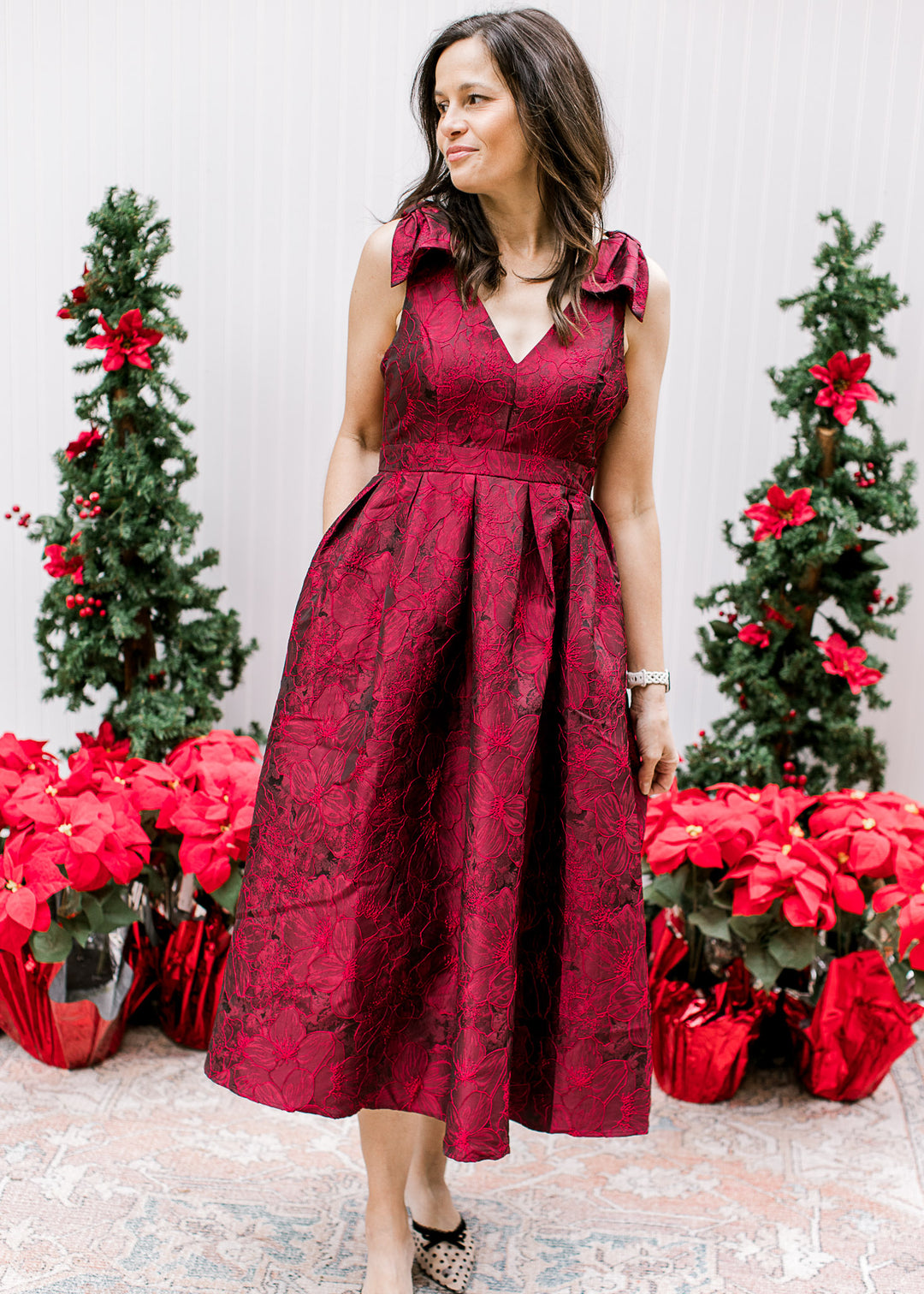 Model wearing a sleeveless wine midi with embroidered floral, pleated waist and a flowy skirt.  