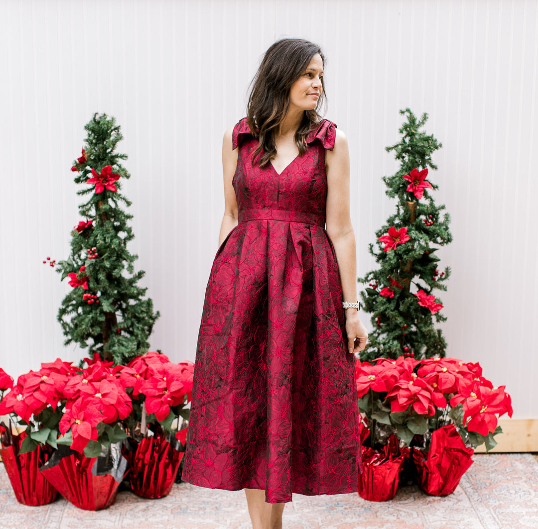 Model wearing a sleeveless wine midi with embroidered floral, pleated waist and a hidden zipper. 