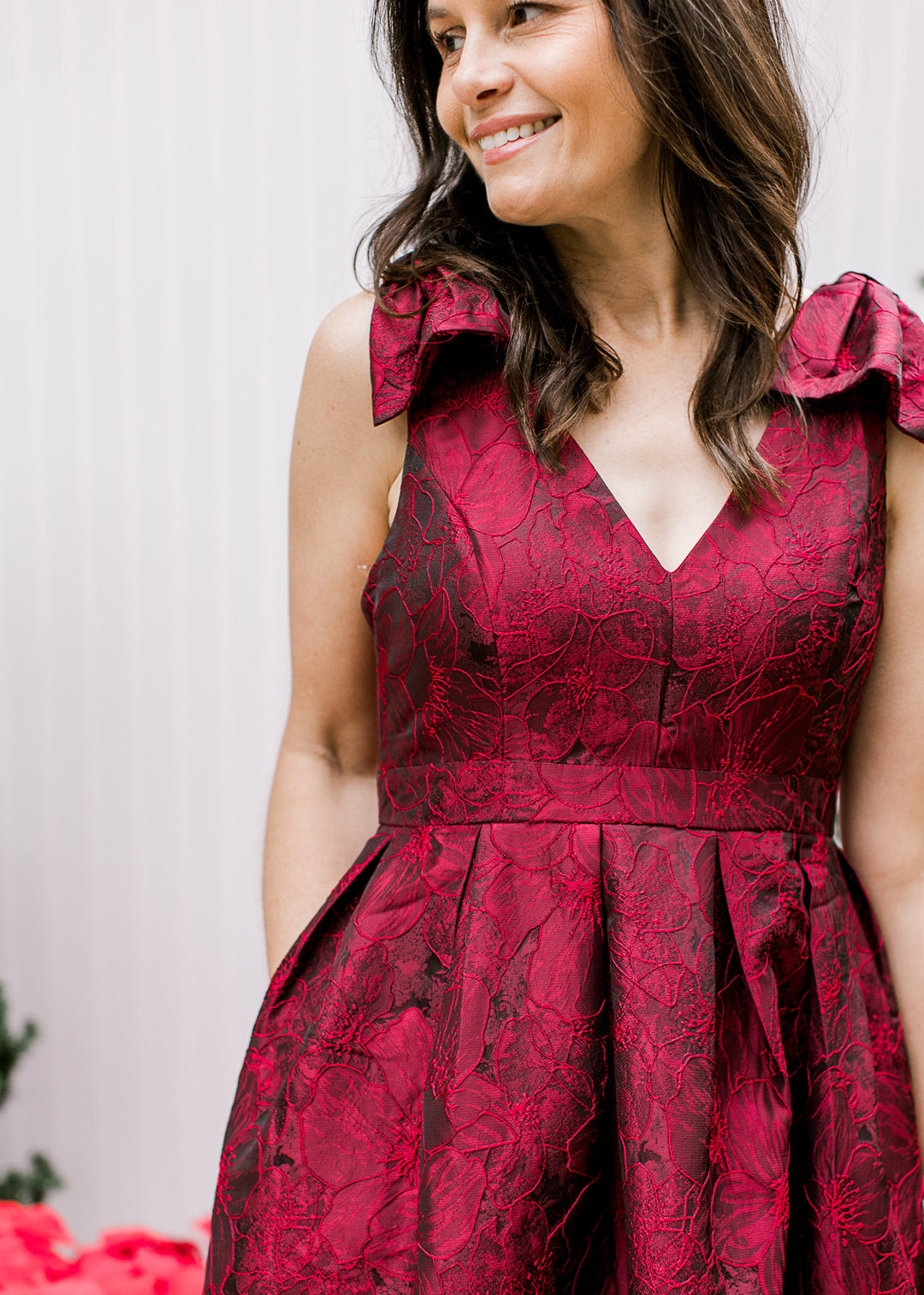 Close up of v-neck and embroidered floral on a wine sleeveless dress with bows at the shoulder. 