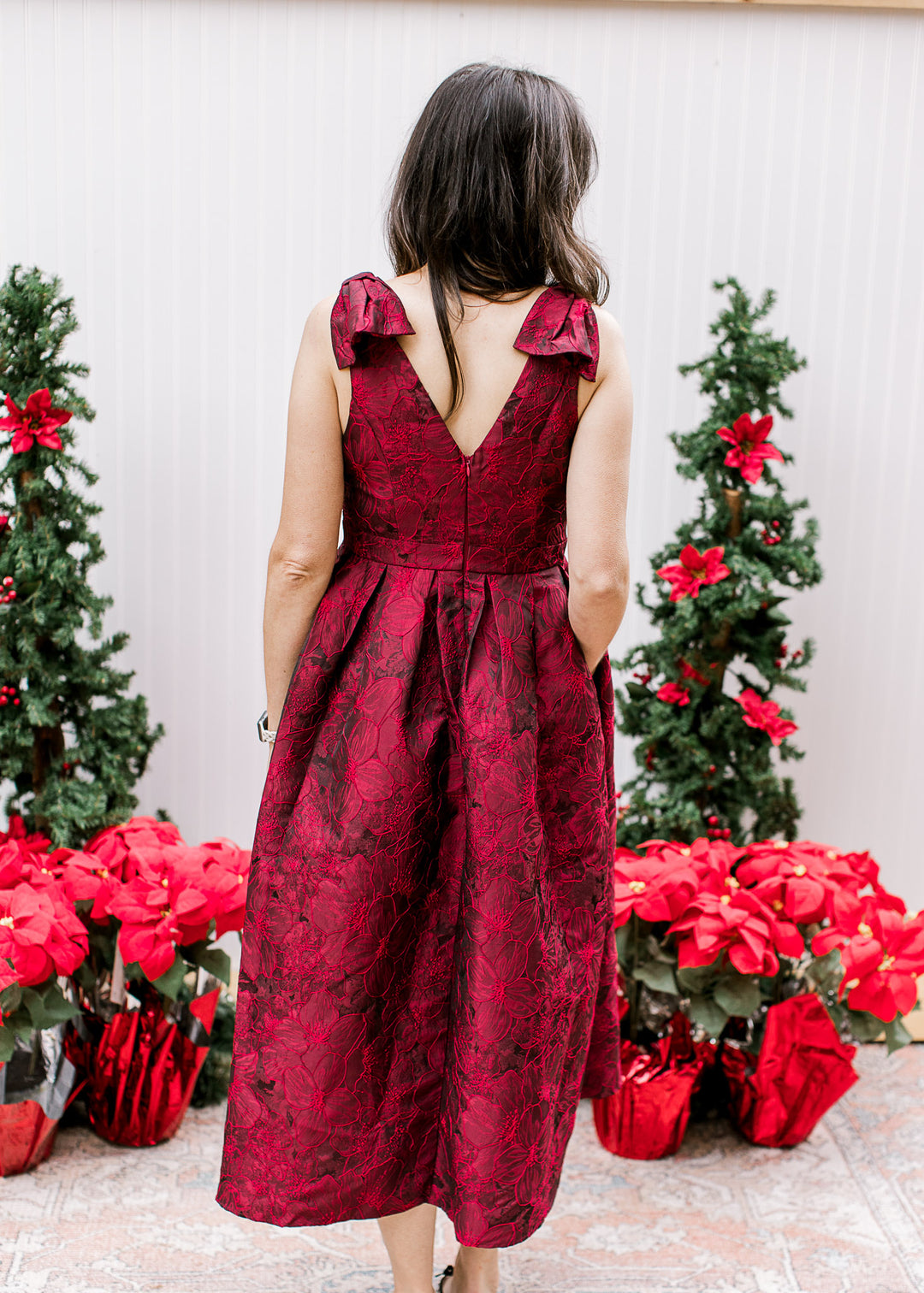 Back view of Model wearing a sleeveless wine midi with embroidered floral and pleated waistline.