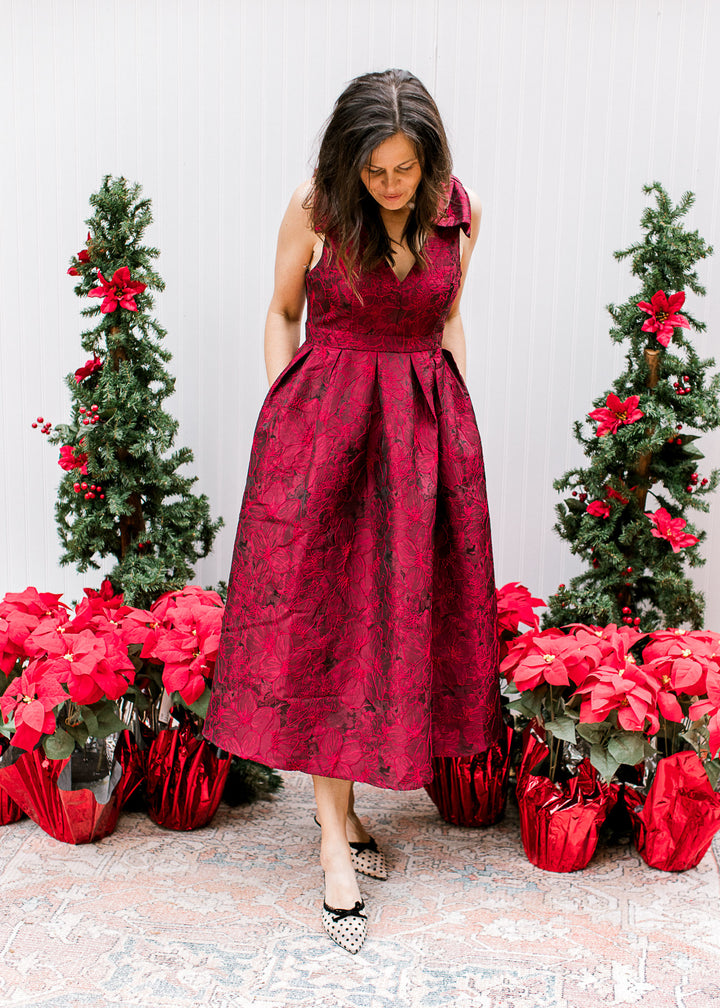 Model wearing low heels and a wine midi with embroidered floral, pleated waist and pockets. 