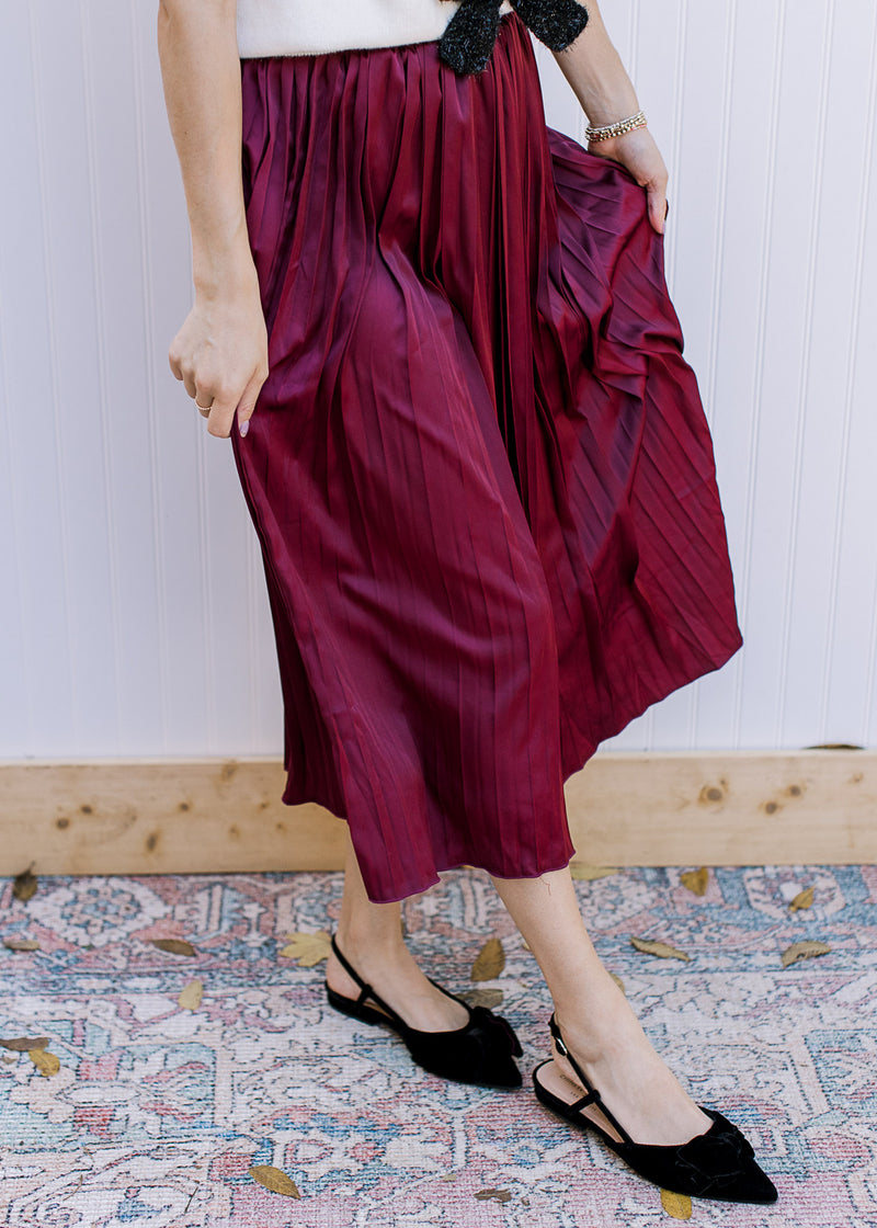 Model wearing a wine colored midi with a satin material, pleating and elastic band. 