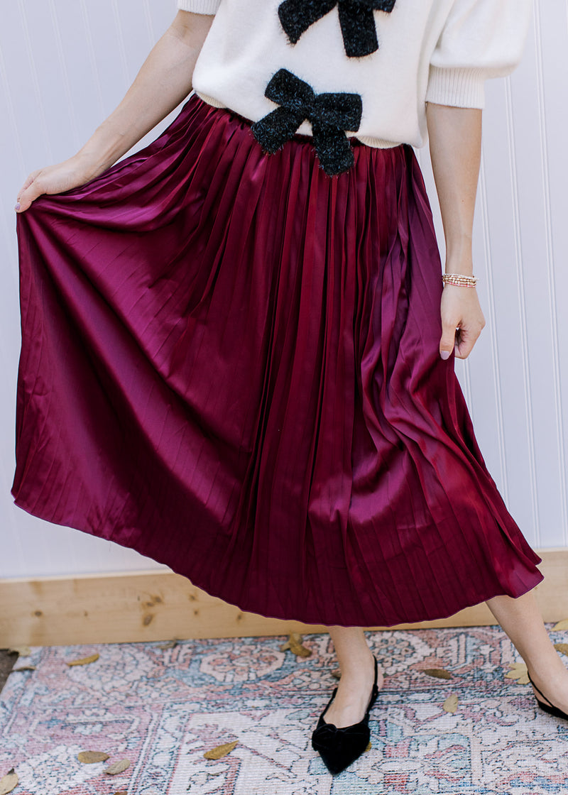 Model wearing black flats and a wine colored midi with a satin material, pleating and elastic band. 