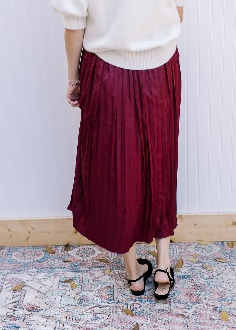 Back view of Model wearing a wine colored midi with a satin material, pleating and elastic band. 