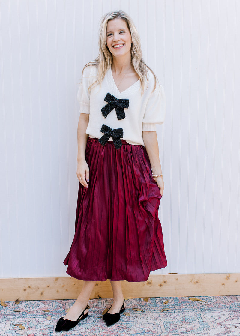 Model wearing a cream top, black flats and a wine colored satin midi with an elastic band. 