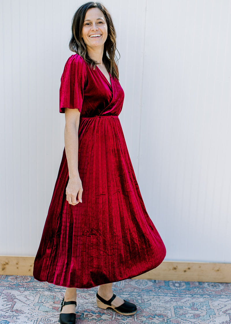 Model wearing a velvet deep wine midi with a pleated skirt short sleeves and faux wrap top. 