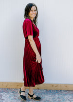 Side view of Model wearing a velvet deep wine midi with a pleated skirt and short sleeves. 