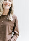 Close up of rolled hem on crew neck of a lightweight brown sweater with long sleeves. 