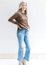 Model wearing jeans and booties with a long sleeve brown sweater with a rolled hem at the neck. 