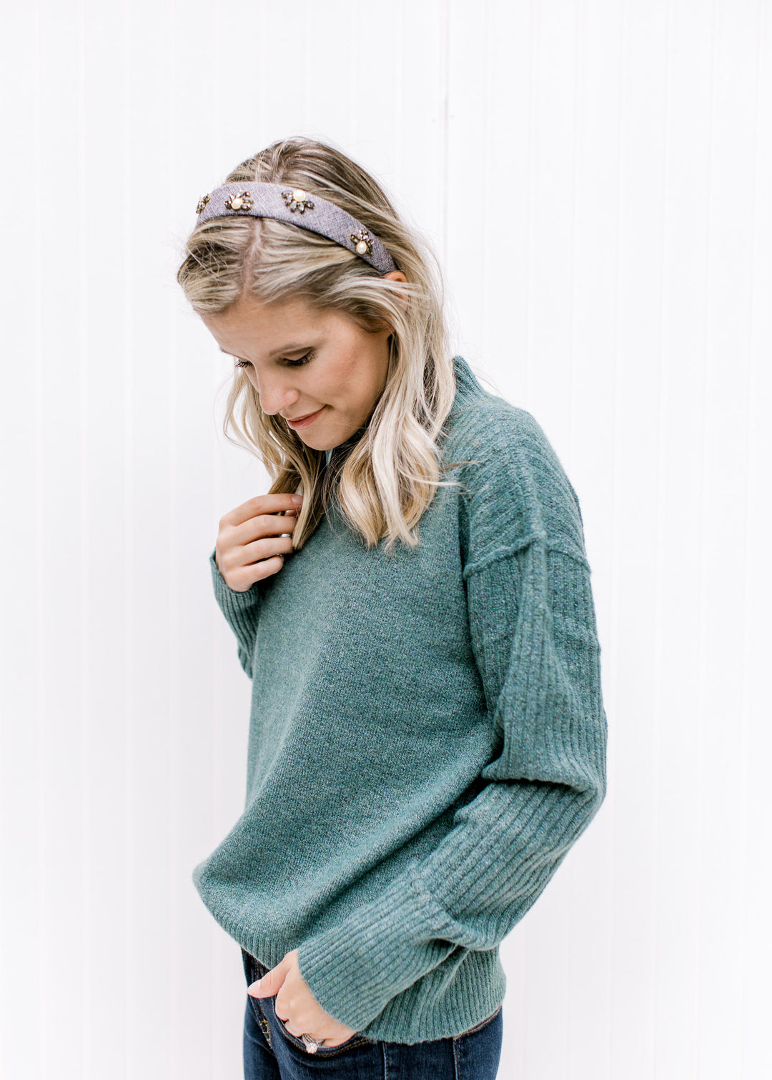 Model wearing a soft forest colored sweater with a mock neck, exposed hem and long sleeves. 