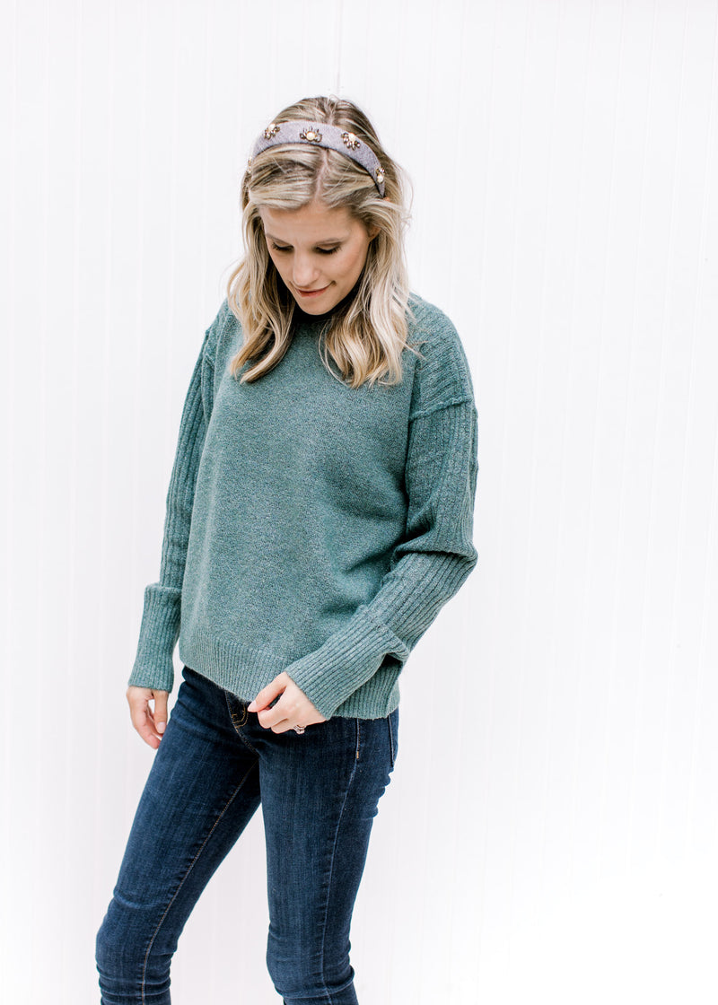 Model wearing jeans and a soft forest sweater with a mock neck, exposed hem and long sleeves. 