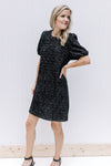 Model wearing a black above the knee dress with white speckles, bubble short sleeve and round neck.