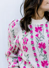 Close up of pink floral pattern on a beige sweater with long sleeves and pleated shoulders. 