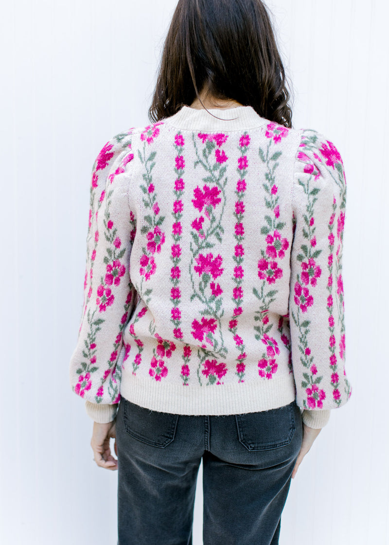 Back view of Model wearing a beige sweater with a pink floral, long sleeves and pleated shoulders.
