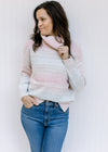Model wearing a long sleeve pink, taupe, aqua and cream ombre sweater with a turtle neck. 