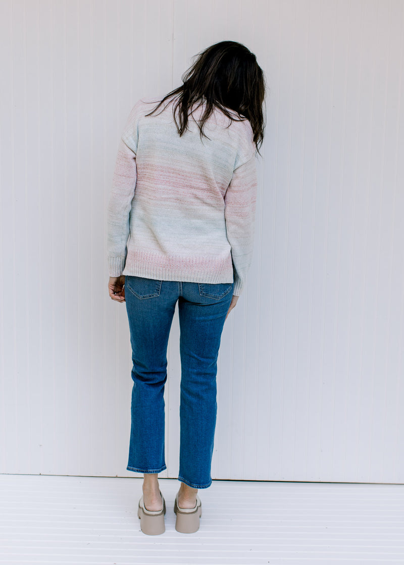 Back view of a model wearing a pink, taupe, aqua and cream ombre sweater with  long sleeves. 
