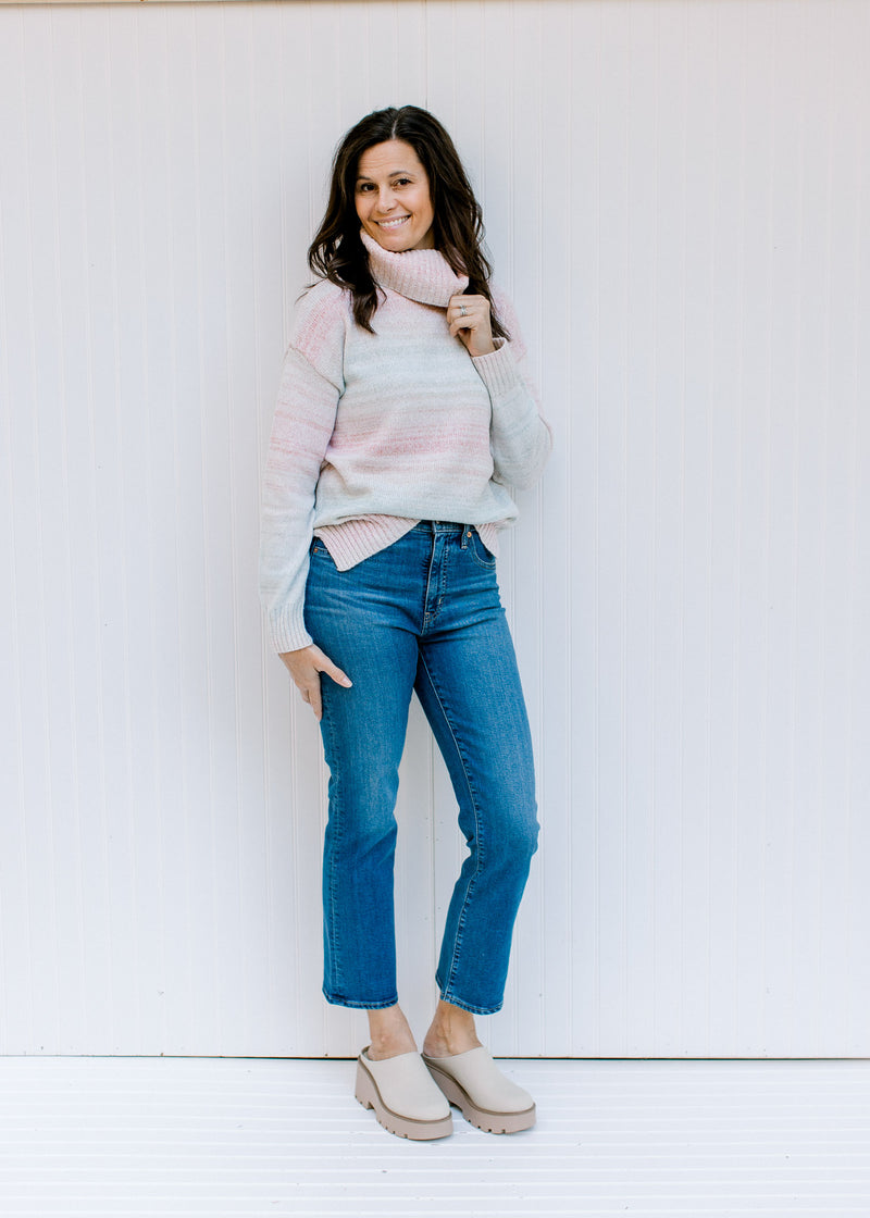Model wearing jeans and mules with a pink, taupe, aqua and cream ombre sweater with long sleeves. 