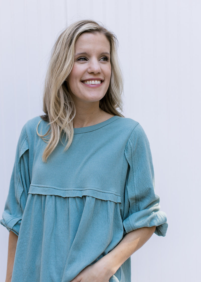 Close up view of fabric detail at arm and bust on a seafoam babydoll top with a round neck. 
