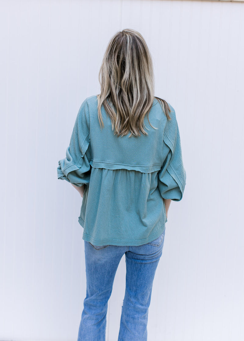 Back view of Model wearing a seafoam babydoll top with a round neck and detail at arm and bust. 