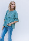 Model wearing a seafoam colored top with a round neck, babydoll fit and detail at arm and bust. 