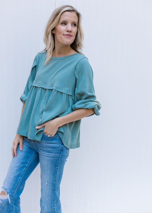 Model wearing a seafoam colored top with a round neck, babydoll fit and detail at arm and bust. 