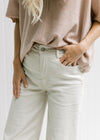 Close up of high waisted fit on a model wearing sand jeans with a tan colored top. 