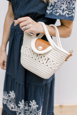 Model holding a woven rope handbag with a pearl closure. 