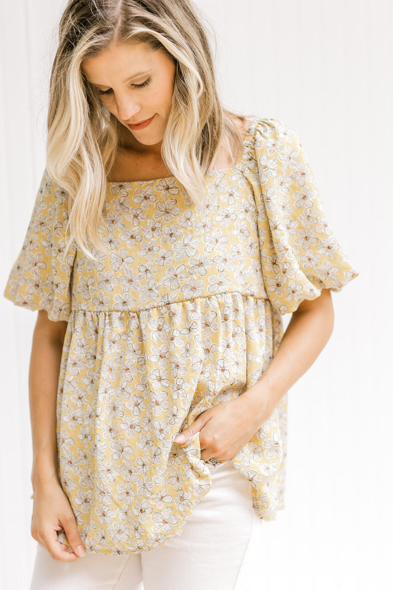 Model wearing a mustard top with a cream floral pattern, square neckline and bubble short sleeves. 