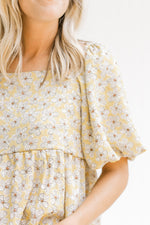 Close up of bubble short sleeves and a babydoll fit on a mustard top with a cream floral pattern. 
