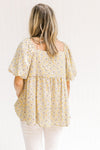 Back view of Model wearing a mustard top with a cream floral pattern, babydoll fit and short sleeves