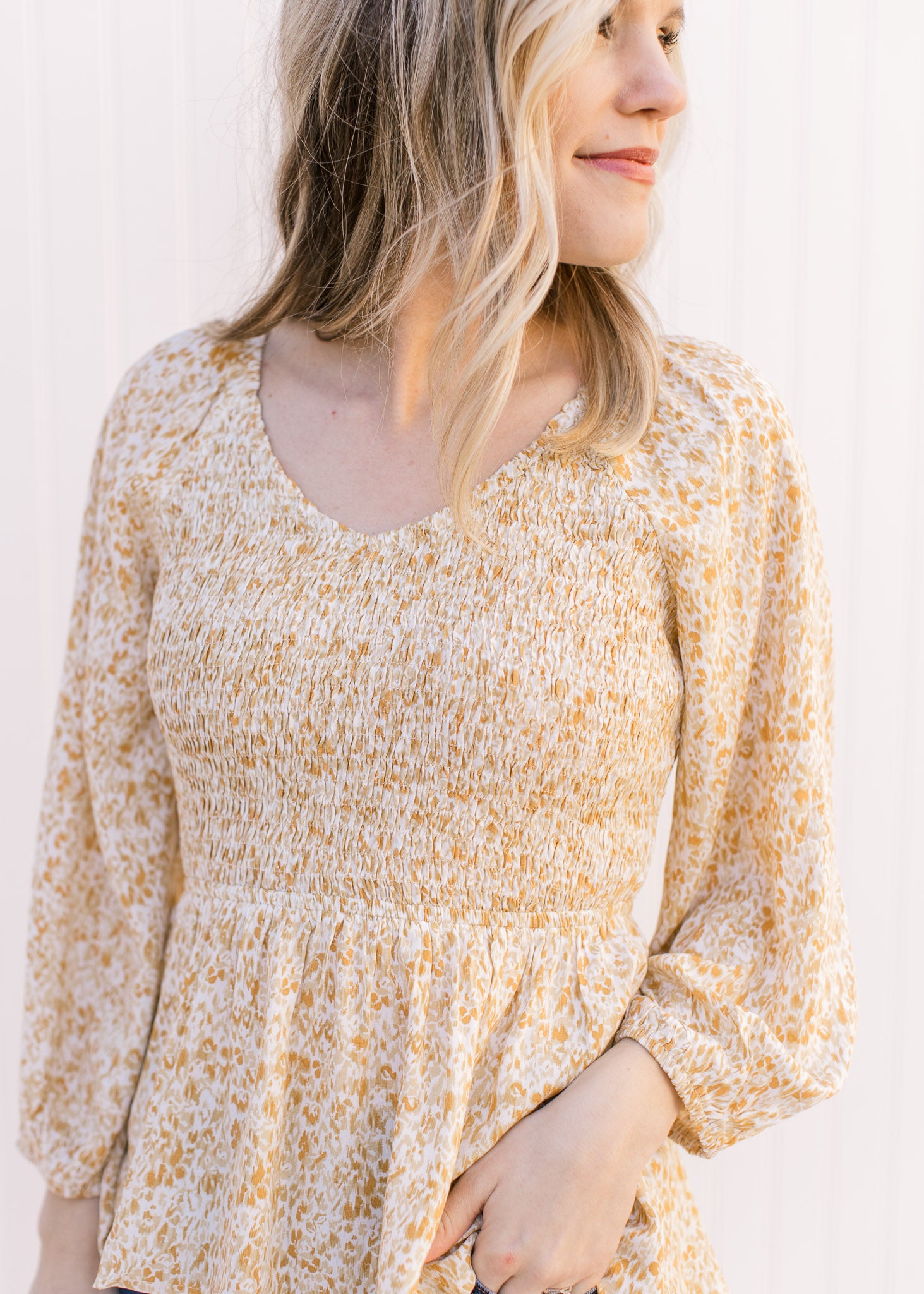 Model wearing a cream top with yellow, cream and gold ditsy floral, a smocked bodice and a v-neck.