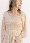 Model wearing a cream top with yellow, cream and gold ditsy floral, a smocked bodice and a v-neck.