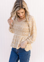 Model wearing a cream top with yellow, cream and gold ditsy floral, smocked bodice and long sleeves.