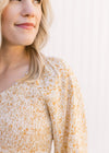 Close up of smocked bodice and v-neck on a cream top with a yellow and gold ditsy floral pattern. 