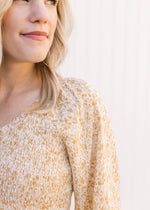 Close up of smocked bodice and v-neck on a cream top with a yellow and gold ditsy floral pattern. 