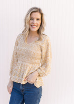 Model wearing jeans with a cream top with yellow, cream and gold ditsy floral, and a smocked bodiCe.