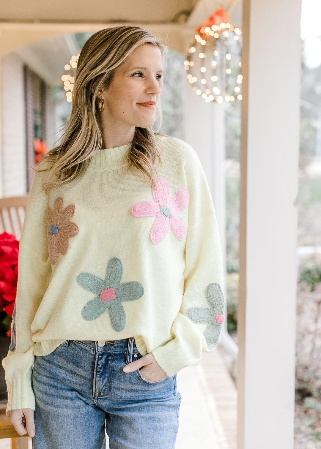 Model wearing a yellow sweater with taupe, pink, and sage flowers, round neck and long sleeves. 