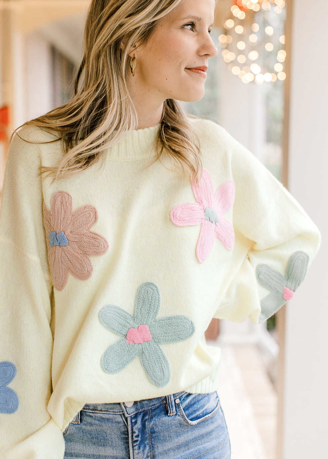 Model wearing a cozy, long sleeve yellow sweater with taupe, pink, and sage flowers  and round neck.