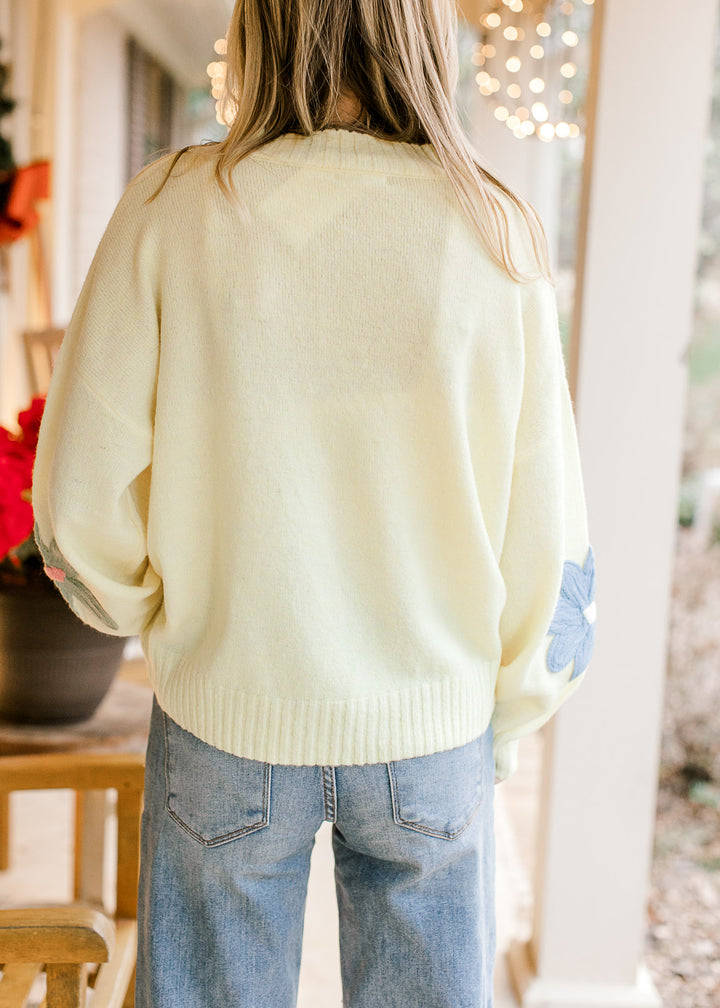 Back view of Model wearing a yellow sweater with flowers, round neck and long sleeves. 