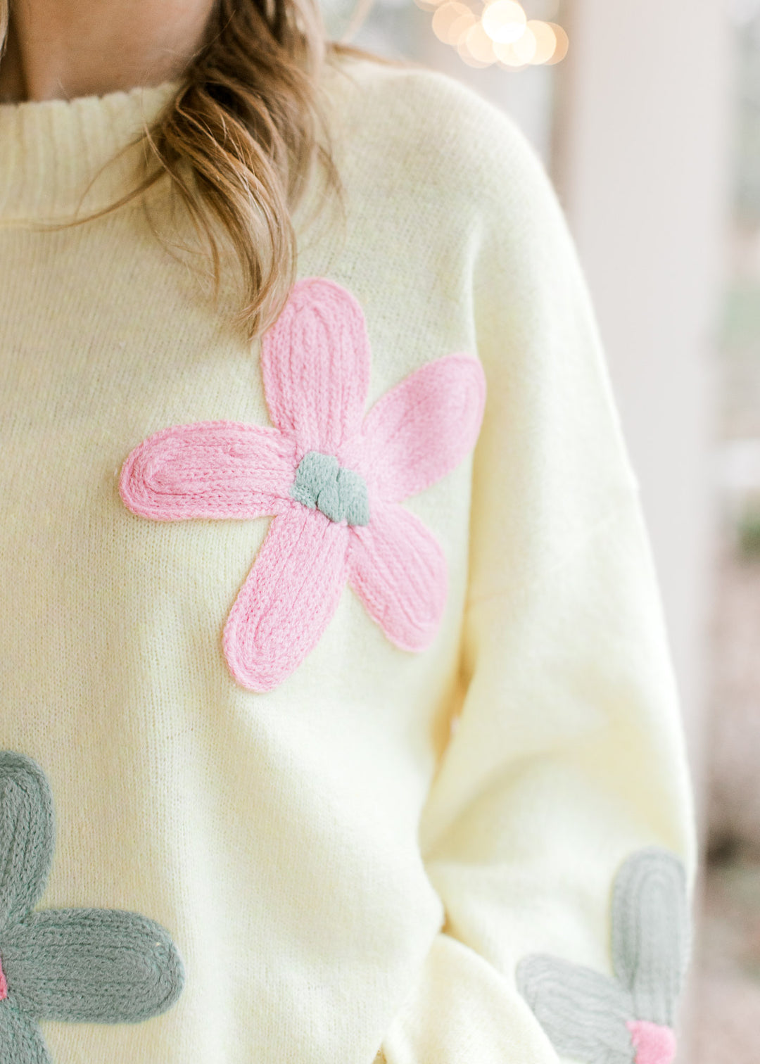 Close up on stitched flower on a yellow sweater with a round neckline and long sleeves. 
