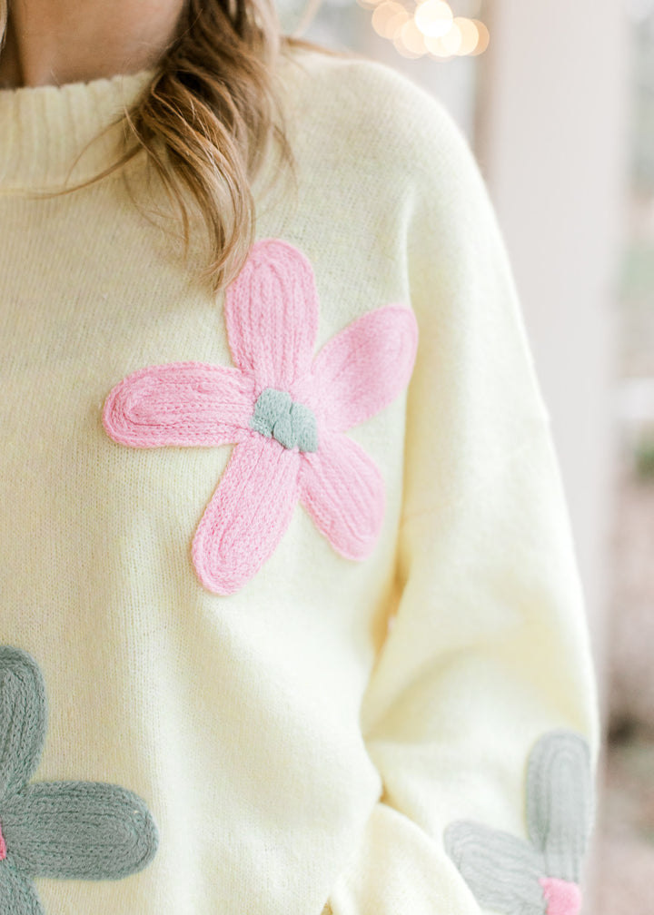 Close up on stitched flower on a yellow sweater with a round neckline and long sleeves. 