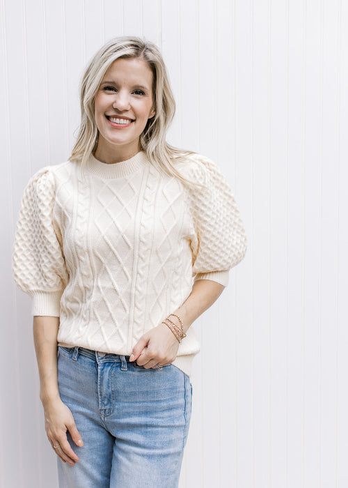 Model wearing a cream yellow sweater with short puff sleeves, cable knit fabric and round neck. 