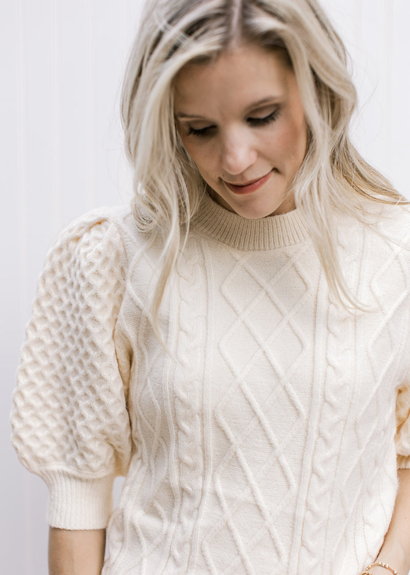 Close up of cable knit fabric and short puff sleeves on a creamy yellow sweater. 