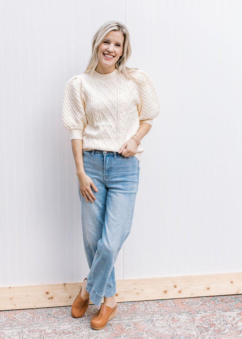 Model wearing jeans, mules and a creamy yellow sweater with short puff sleeves. 