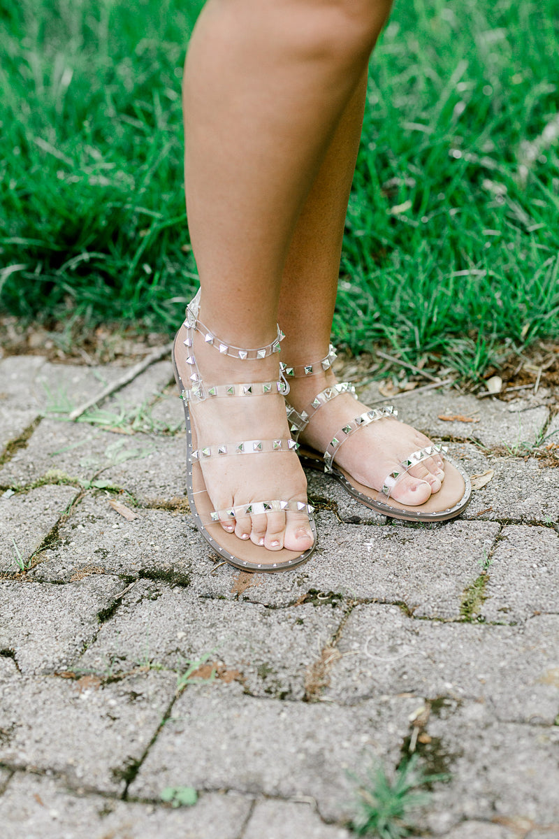 A pair of clear lucite sandals with silver stud on model.