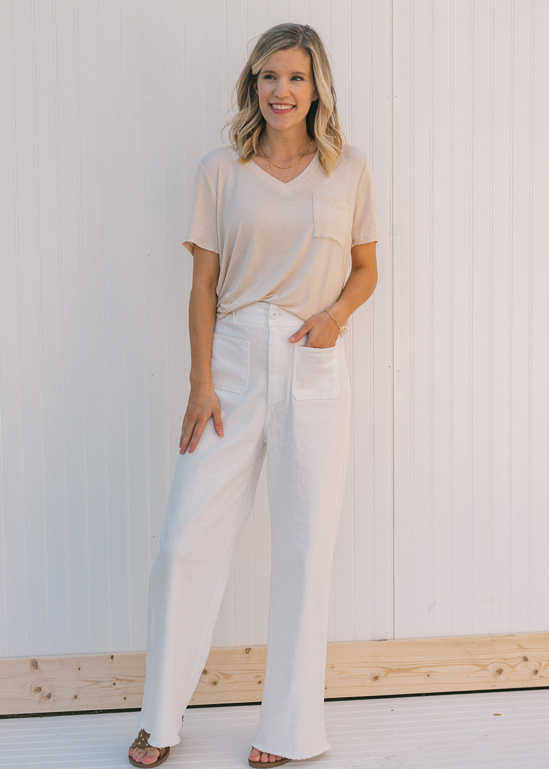 Model wearing a cream, short sleeve tee with a front pouch pocket and white pants. 