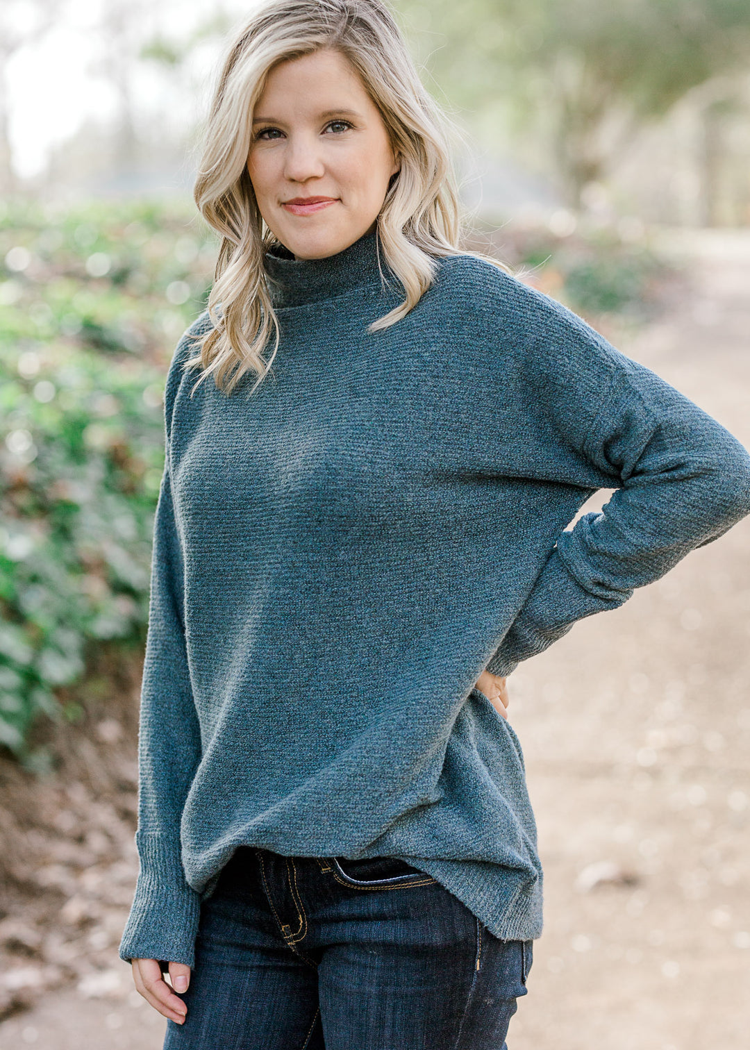 Blonde model wearing a teal sweater with a mocked neck. 